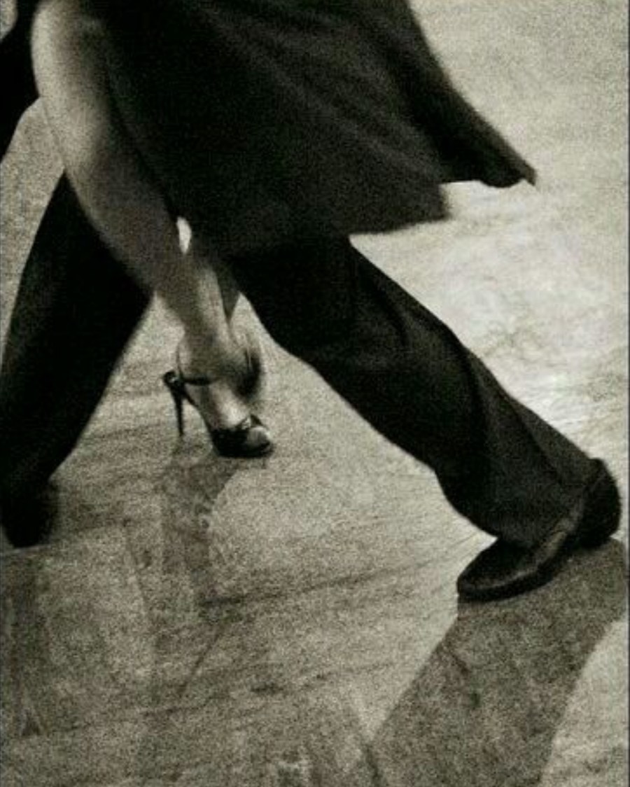 A black-and-white photograph of two dancers' legs mid-tango, one in heels