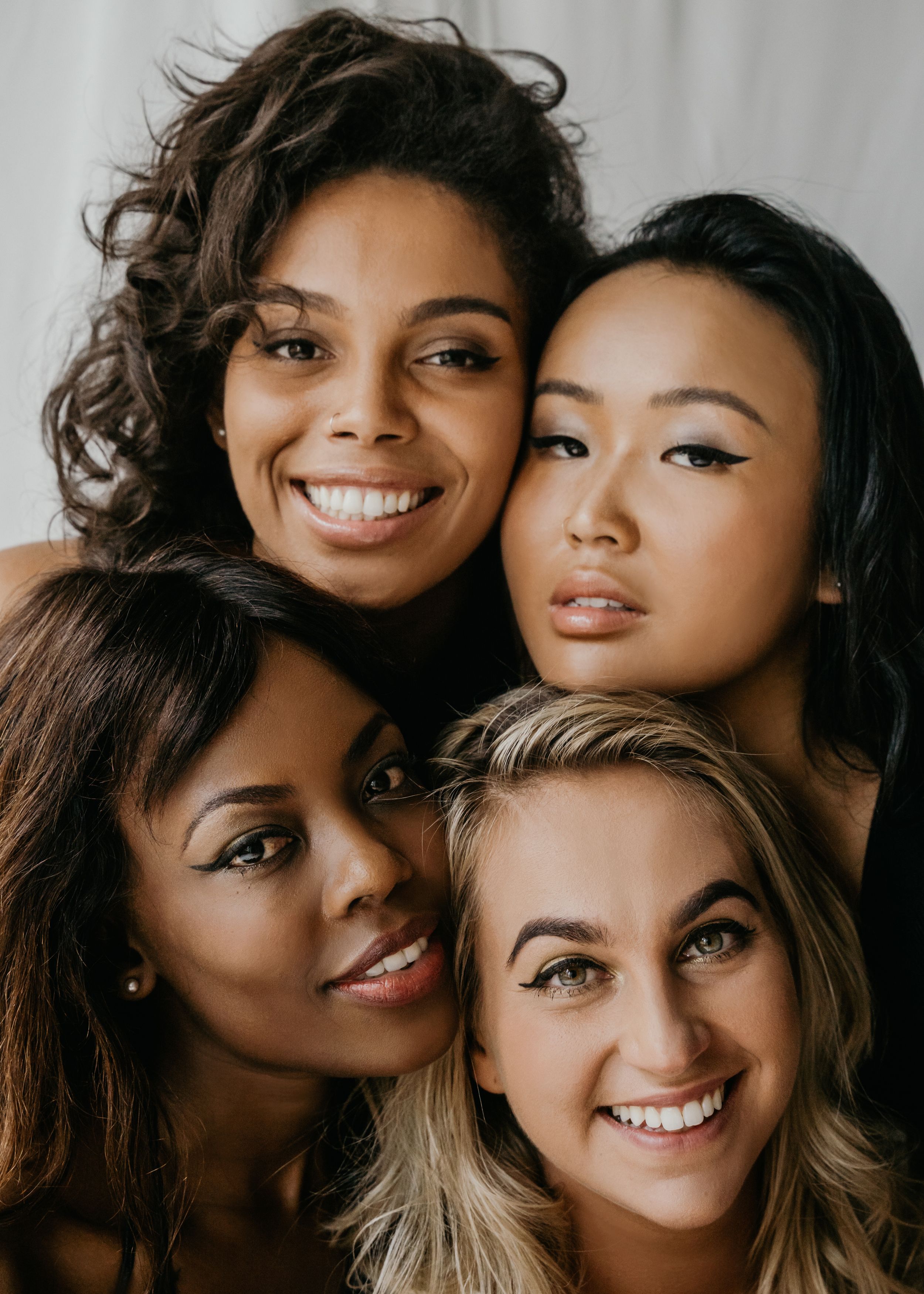 Four women with their faces close together, smiling toward the camera
